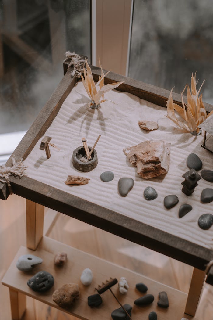 Minimalist indoor zen garden with rocks, sand, and plants on a wooden table.